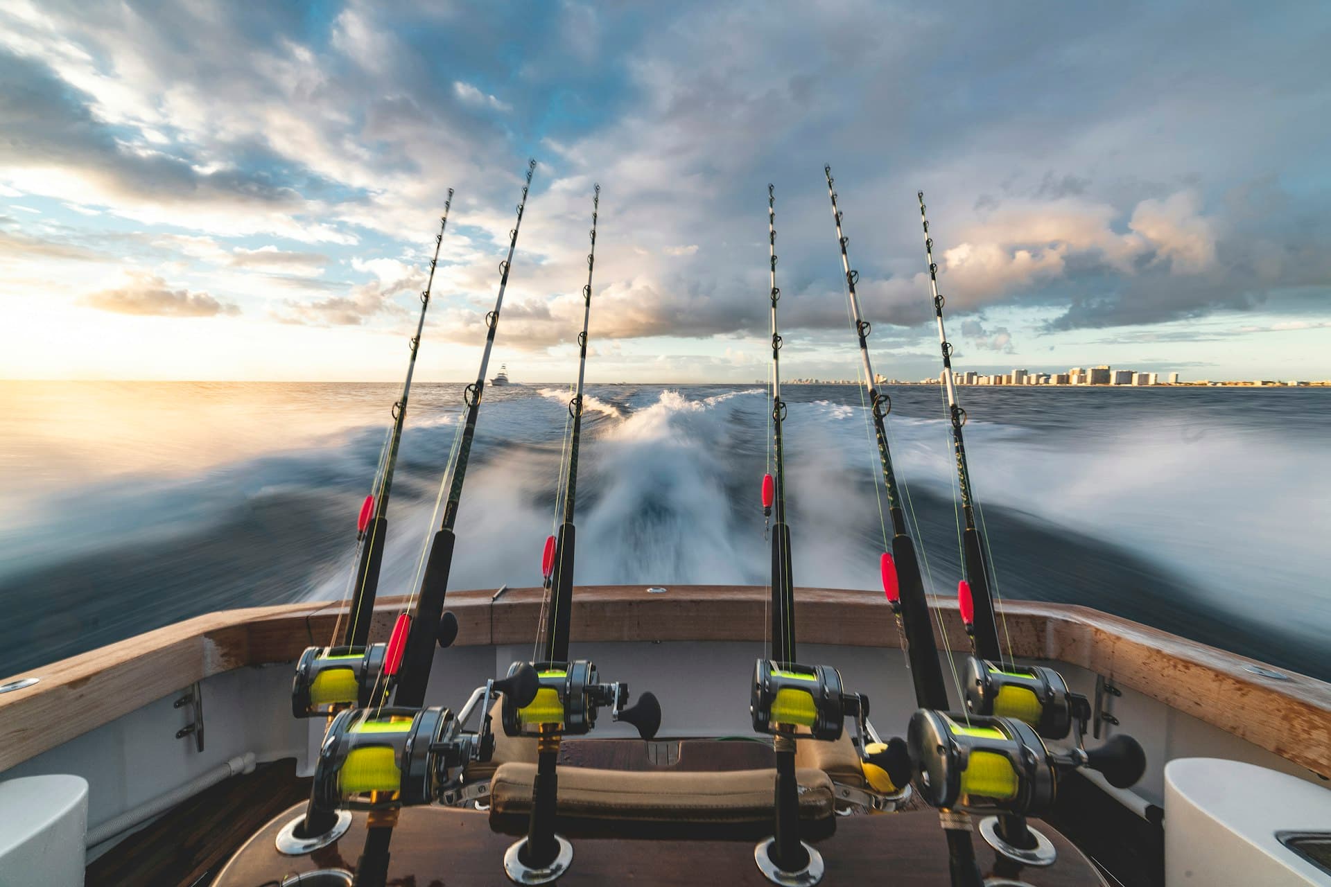 Fishing rods on the back of a boat running out to sea at sunrise